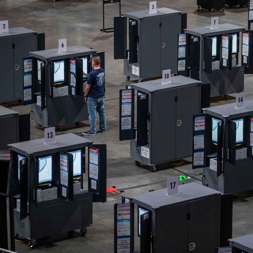 Several large metal cabinets with screens are lined up in a large hall. One person is touching one of the screens.