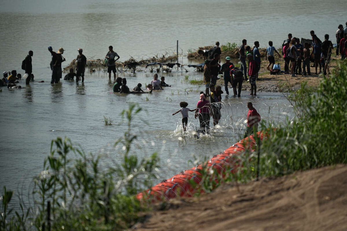 Migrants cool themselves in the waters of the Rio Grande after crossing to the U.S. from Mexico near a site where the state is installing large buoys to be used as a border barrier along the Rio Grande near Eagle Pass, Texas, Monday, July 10, 2023. (AP Photo/Eric Gay)