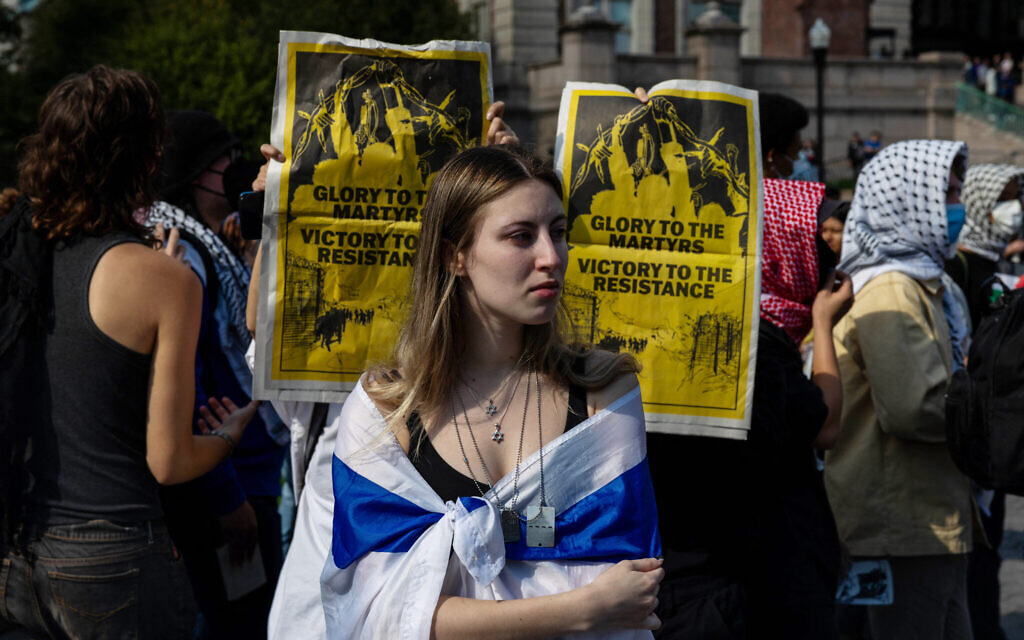 Anti-Israel protesters hold up posters behind a student attending a rally to mourn victims on the one-year anniversary of the October 7 Hamas terror onslaught, on October 7, 2024 in New York City. (Photo by Alex Kent / GETTY IMAGES NORTH AMERICA / Getty Images via AFP)