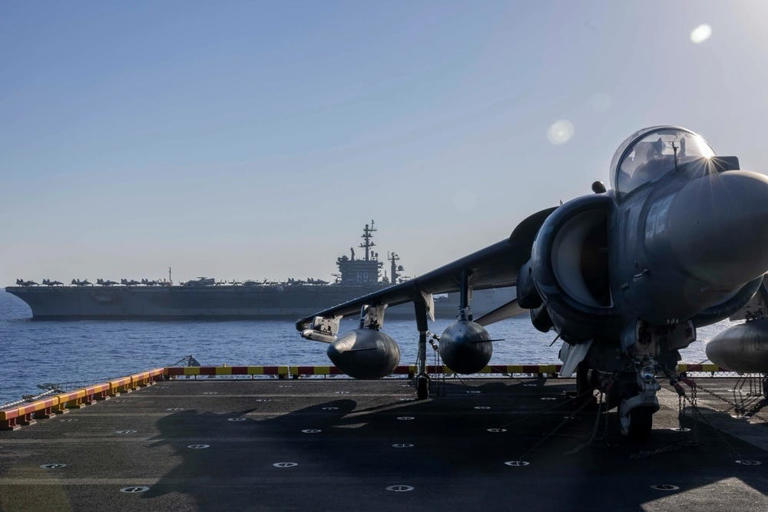 A fighter jet is seen aboard the amphibious assault ship USS Wasp with the aircraft carrier USS Dwight D. Eisenhower in the distance. US Navy photo by Mass Communication Specialist 2nd Class Sydney Milligan